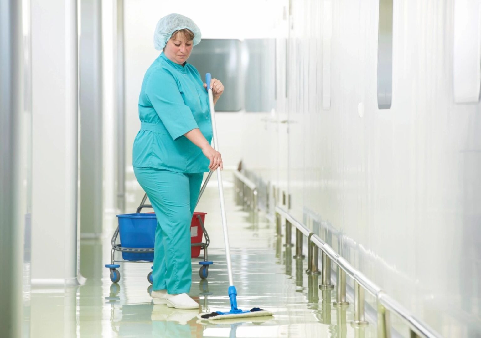 A woman in scrubs mopping the floor of an industrial building.