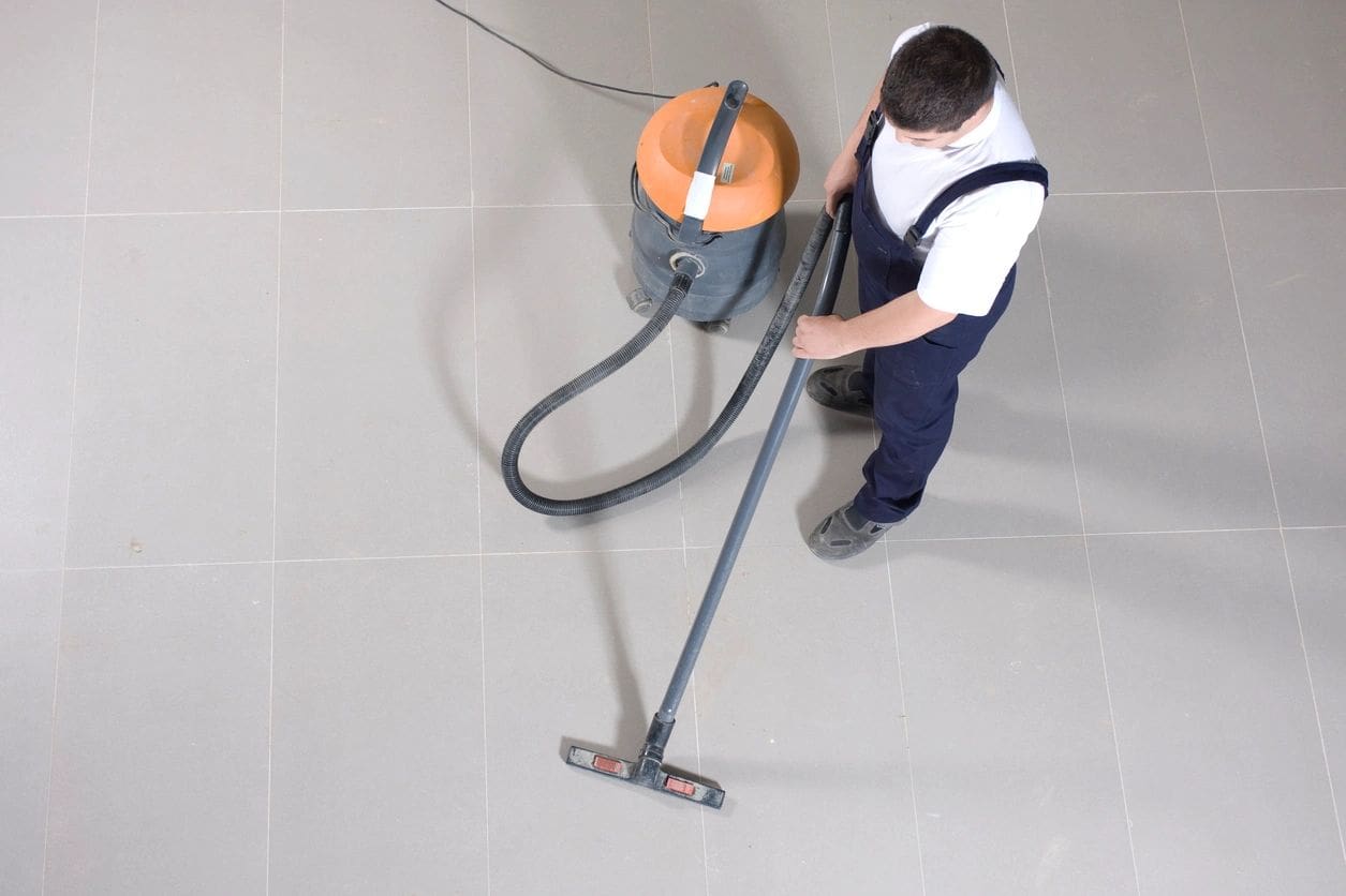 A man is vacuuming the floor with an orange vacuum.
